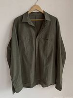 Front view of greenish Lululemon men's button-up shirt on hanger, long sleeves, two chest pockets, button cuffs.