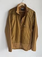 Full view of the men's Orage large zip-up jacket, hung on a wooden hanger against a white wall shows its brown color and waffle knit sleeves.