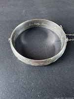 Front view of the wide sterling silver bangle bracelet showing embossed floral pattern and partial view of engraved inscription inside.