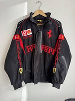 Front view of black Ferrari racing jacket showing Ferrari logo, Shell and Vodafone patches