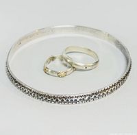 Photo showing the three jewelry items including sterling silver bangle with beadwork detail and two silver rings, one plain and one floral patterned