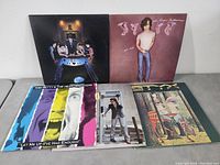 Five classic rock vinyl records spread out on a gray surface showing the album covers including Elvis Costello and John Mellencamp.