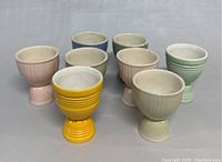 Nine Mid-Century Modern ceramic double egg cups arranged in rows by color, showing different pastel shades and one bright yellow cup.