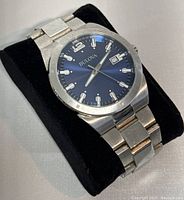 Watch on black display stand showing blue dial, silver-tone hands and hour markers