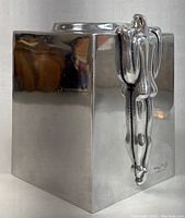 Front and side view of the silver-tone metal cube tissue box holder with sculptural human figure decoration and signature mark.
