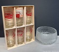 Six TTC drinking glasses in original packaging next to a clear textured glass salad bowl.