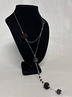 Front view of the modernist necklace displayed on a black stand, showing the asymmetrical arrangement of raspberry cluster beads and chain drops