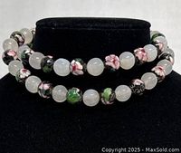 Close-up photograph showing the detailed cloisonne beads with pink and white flowers on a black background interspersed with smooth white beads.
