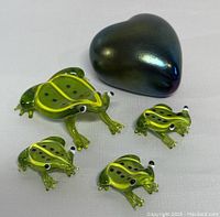 Four green art glass frogs of different sizes, one large with a minor chip and three smaller ones, all translucent with black spots and detailed eyes and toes