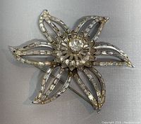 Front view of vintage CORO brooch showing silver-tone flower design with clear rhinestones accenting five petals and center cluster.