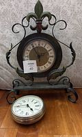 Photo of two clocks: a decorative fleur-de-lis metal stand clock and a vintage metal pocket watch style clock