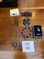 Photo showing various jewellery including 2 necklaces with pendants, a bead bracelet, a black beaded ornate brooch or cuff, a decorative pouch, and a small boxed Swarovski pendant necklace.