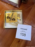 Box set showing various gold-tone tie clips and a pair of cuff links with a matching tie clip on a yellow card.