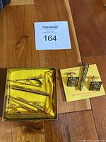 Box with five assorted gold-tone tie clips displayed on yellow satin lining.