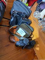Photo showing Bushnell binoculars with carrying case and other equipment on wooden floor.