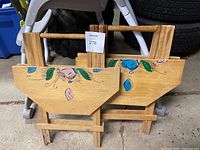 Two wooden fold-up tables folded flat, front view showing floral designs.