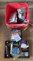 Bucket with large metal pipe fittings, voltage detector packaging, and red reflector visible with other assorted items in a black tray.