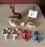 Wood sitting deer sculpture, multiple natural decorative stones, and four metal wall hooks arranged on a table.