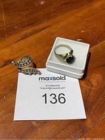 Two 925 sterling silver rings displayed on a wooden surface and one ring placed in a white jewelry box.