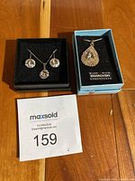 Two jewelry sets with boxes on wooden surface, Swarovski set on blue box, Levien set on black box with necklace and earrings.