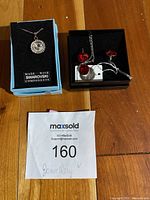 Lot displayed on wooden surface showing the blue Swarovski component box containing the silver-tone crystal pendant necklace and a black box with red crystal earrings and matching necklace, along with lot information sheet.