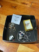 Photo showing 3 cat-themed necklaces and a small yellow box containing cat-themed earrings and a pendant charm inside a black tray