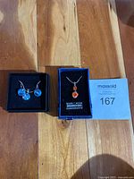 Both jewelry sets displayed on wooden floor, showing the orange heart pendant necklace and the baby blue crystal earring and necklace set.