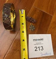 View of the set showing the bangle bracelet, pin, and charm next to a measuring tape for size reference.