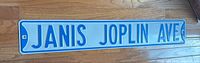 Full view of the Janis Joplin Ave. street sign lying on a wood floor showing the entire sign and mounting hole on each end.