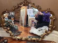 Oval ornate gold-framed mirror reflecting room and person taking photo