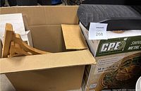 Partially opened box showing decorative wooden hose hanger brackets inside and boxed metal hose reel below.