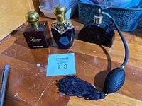 Three vintage perfume bottles on wooden table, including Lauren Ralph Lauren cologne bottle, blue bottle with gold rose trim, and black atomizer bottle with tassel.
