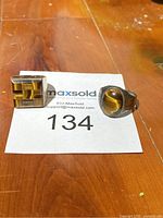 Two sterling silver rings: one with an oval Tiger's Eye stone, the other with a geometric silver design on a wooden surface.