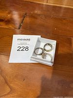 Three rings in a small white box on wooden surface seen from above. Includes flower ring, gold symbol ring, and Celtic knot ring.