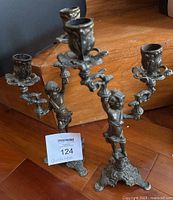 Pair of vintage brass candelabras showing sculpted child figure holding candle holders with ornate bases on wooden floor.
