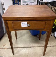 Front view of closed wooden sewing table showing drawer and tapered legs