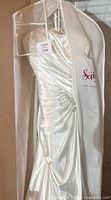 Full view of ivory satin wedding dress with sweetheart neckline inside a cloth garment bag