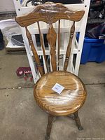 Full front view of the wooden chair showing the carved backrest, spindle supports, round seat, and decorative metal feet. Tape is applied on top of the backrest.