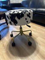 Full view of the stool showing black and white faux cowhide round seat, gold-toned adjustable base with caster wheels.