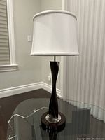 Full front view of the Helix tall table lamp showing the white fabric shade and twisted dark walnut wood body on a glass table.