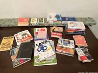 Full assortment of approximately 20 books spread on table, showing diverse sizes, covers, and mostly Japanese titles.