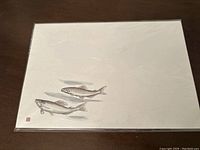 Photo of Japanese calligraphy writing paper sheet with a print of two fish swimming, set against an off-white background.