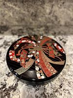 Top view of the round lacquerware dish showing detailed decorative pattern in red, gold, and black.