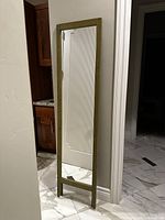 Full view of the large full-length green wooden mirror standing on a marble floor against a wall.