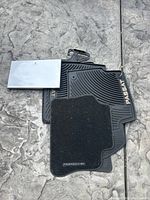 Two Volkswagen Passat black rubber floor mats stacked with a smaller black Porsche carpet floor mat on top, all on a stone surface.