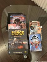 Overview of the lot showing Star Wars Force and Destiny Knights of Fate book, Starfinder book, Werewolf The Forsaken book, Dungeon and Dragons book, Final Fantasy video game case, and City of Heroes video game case on a glass table.