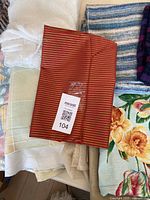 View of assorted fabric pieces including red and gold striped fabric, white netted fabric, blue and white textured fabric, and cream/off-white fabrics stacked together.