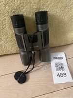 Front view of Meade binoculars showing lenses, rubber eyepieces, and attached wrist strap.