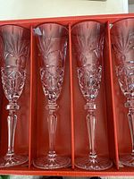 Four identical crystal champagne flutes with detailed cut-glass designs displayed upright in an orange compartmented tray.