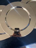Single gold-tone charger plate with reflective surface photographed on black background.